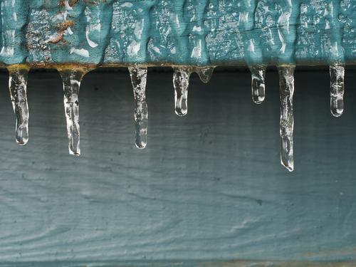 The aftermath of some freezing rain and temperatures. Small icicles hang in a row from a wooden painted deck rail.