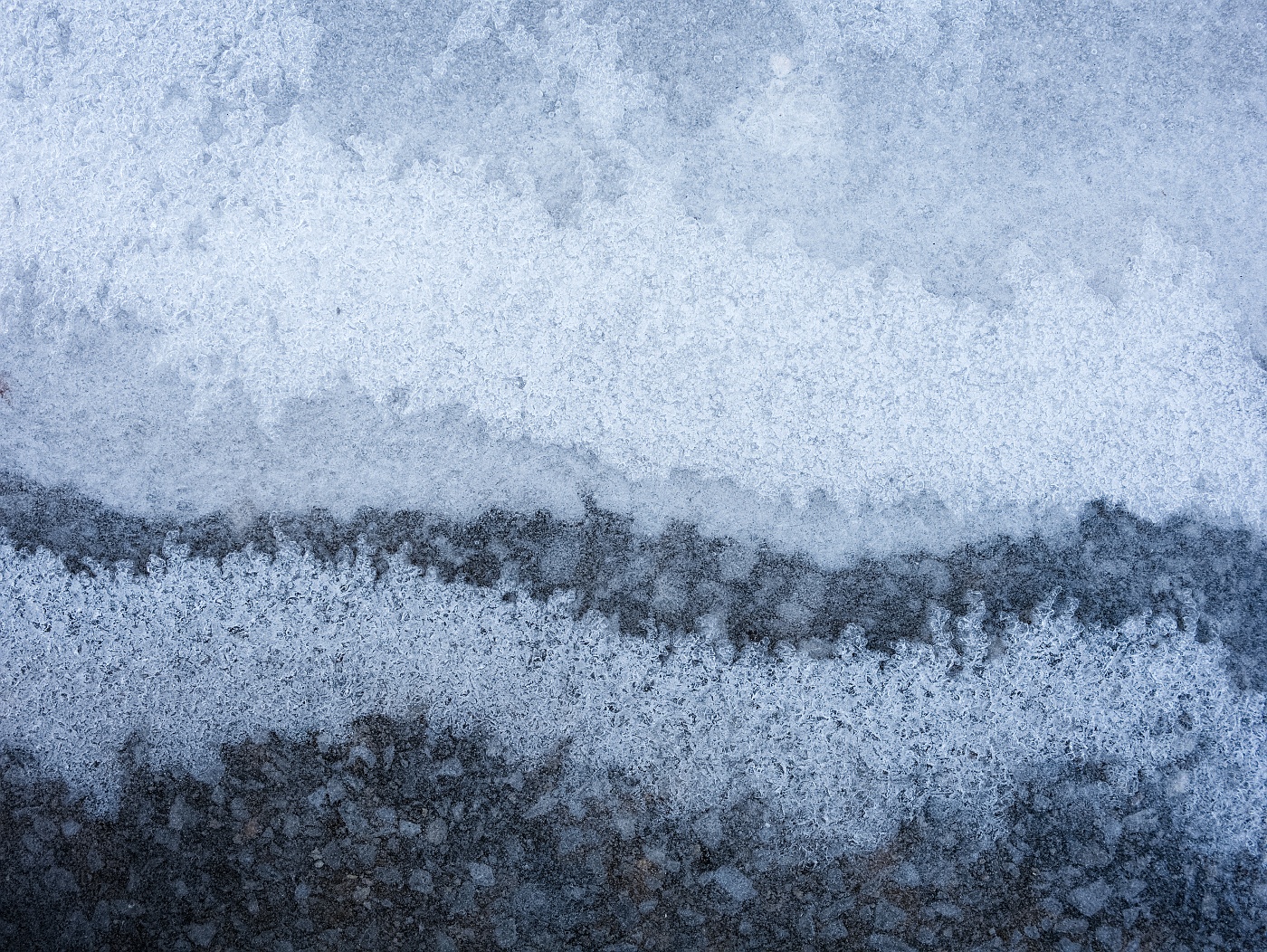 Ice covering asphalt, forming a series of bands of darker and lighter areas where the ice thickness differs.